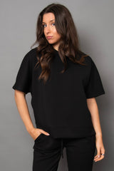 Woman wearing a black t-shirt and pants against a gray background