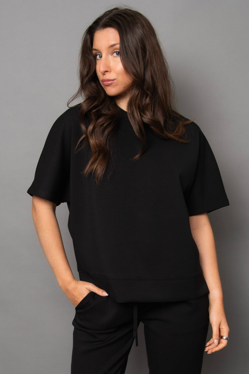 Woman wearing a black t-shirt and pants against a gray background