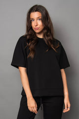 Woman wearing a black t-shirt and pants against a gray background