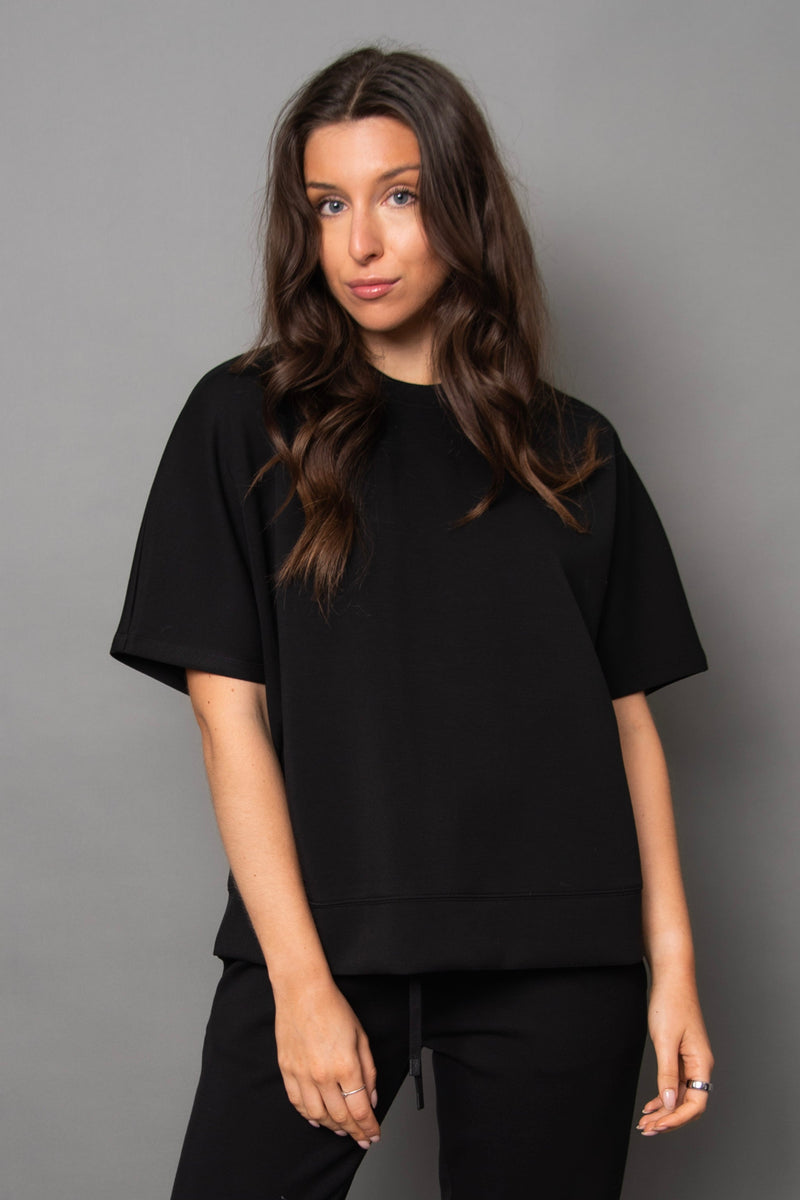 Woman wearing a black t-shirt and pants against a gray background