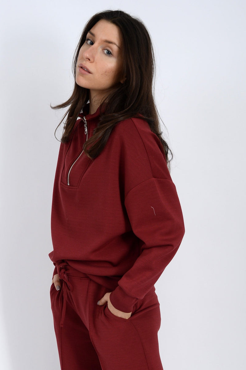 Woman wearing a burgundy tracksuit against a white background.