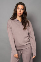 Woman wearing a light beige/grey tracksuit against a gray background
