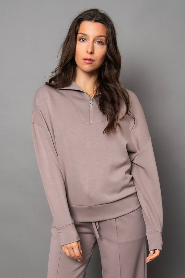 Woman wearing a light beige/grey tracksuit against a gray background