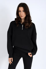Woman wearing a black outfit with a quarter-zip top on a white background