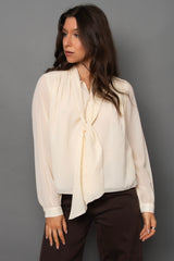 Woman wearing a cream blouse with a tie detail against a gray background