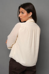 Woman wearing a cream blouse against a gray background