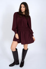Woman wearing a burgundy dress with long sleeves and black knee-high boots on a white background