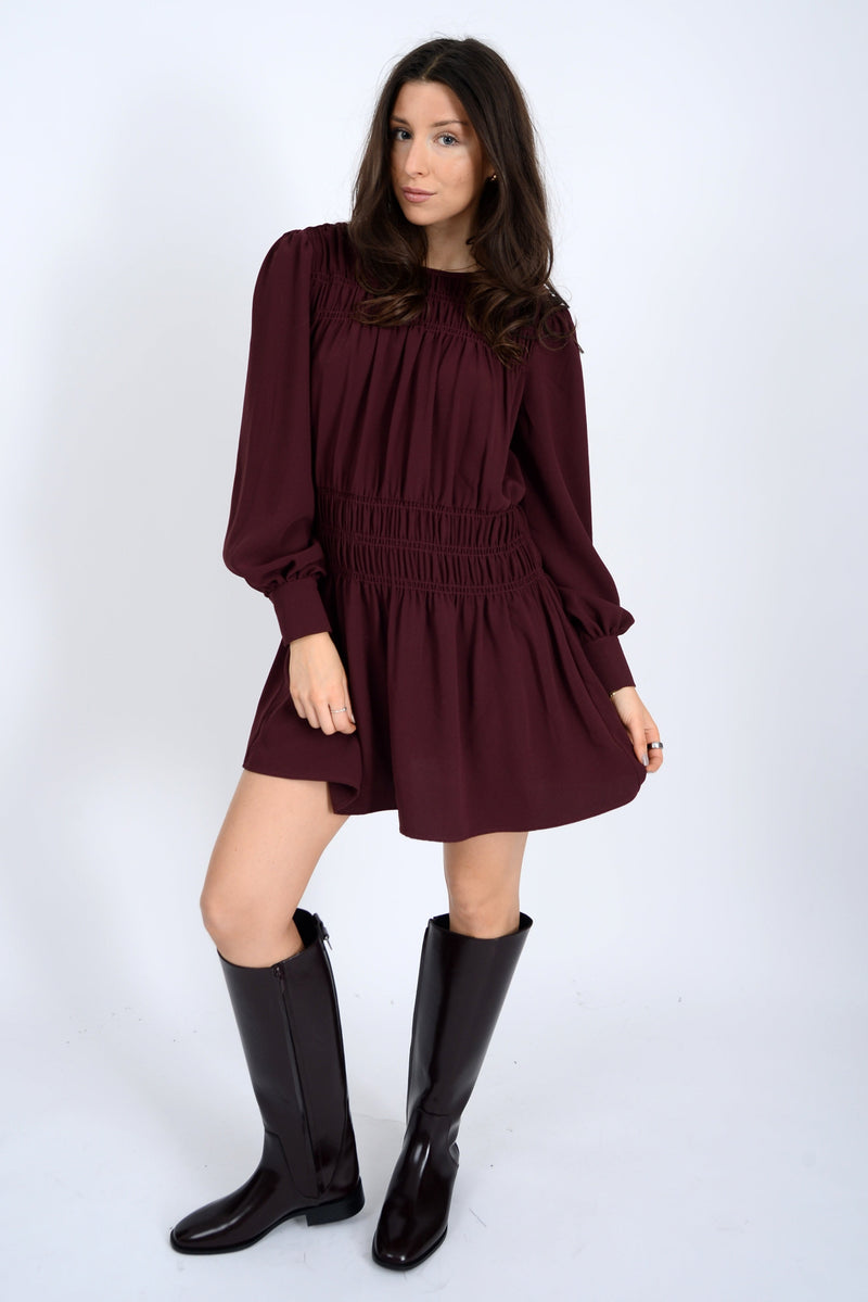 Woman wearing a burgundy dress with long sleeves and black knee-high boots on a white background